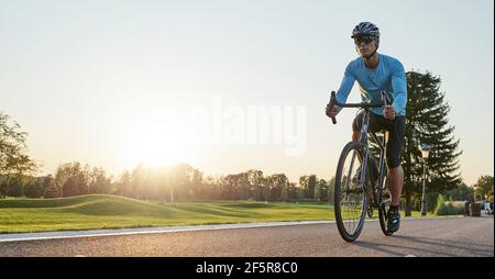 Encabezado del sitio web de la vista trasera del hombre atlético en sportswear de pie con la bicicleta en la carretera. Montar en bicicleta de montaña en un soleado día de verano Foto de stock