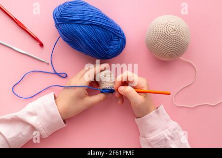 Las manos de los niños en el proceso de crocheting juguetes de hilo azul y beige.