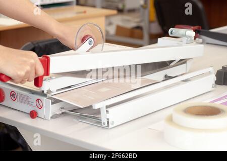 mujer de cerca con dos manos trabajando en una guillotina manual para papel en una fábrica de impresión o en una oficina Foto de stock