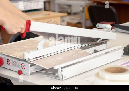 primer plano la mano de una mujer corta una hoja laminada con un guillotina para papel en una imprenta o en un fábrica Foto de stock