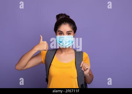Mujer estudiante India en máscara médica mostrando pulgares hacia arriba gesto Foto de stock