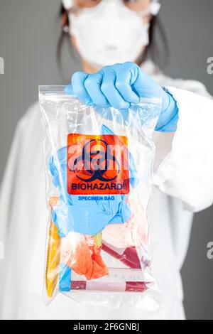 Una investigadora mujer está sosteniendo una bolsa de plástico transparente con el logotipo de peligro biológico impreso. La bolsa contiene especímenes biológicos potencialmente peligrosos. Scient Foto de stock