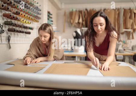retrato de dos jóvenes bellas mujeres sastres o diseñadores de moda trabajar con patrones de ropa en el taller de estudio mientras se costura clásica pantalones adentro