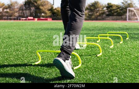 Los pies de un atleta pisando sobre las barreras amarillas mini bananas establecieron aon un campo de césped verde para ejercicios de entrenamiento deportivo.