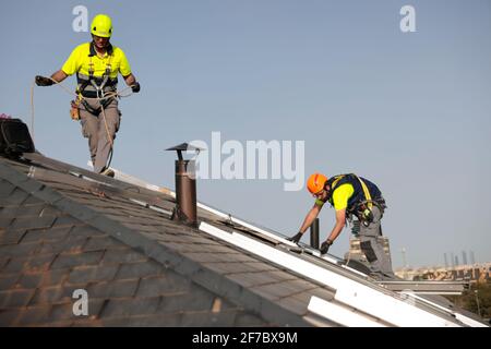 Los trabajadores que usan máscaras instalan paneles solares en un techo de una casa residencial en Majadahonda, Madrid, España. Foto de stock