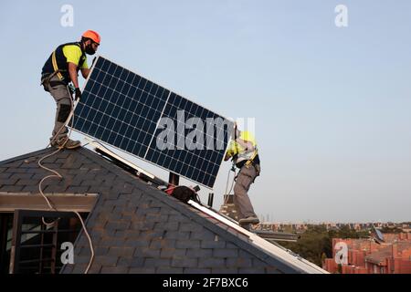 Los trabajadores que usan máscaras instalan paneles solares en un techo de una casa residencial en Majadahonda, Madrid, España. Foto de stock