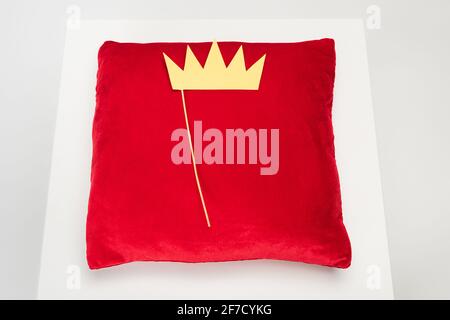 vista superior de la corona de papel amarilla en el palo y rojo almohada de terciopelo en gris Foto de stock