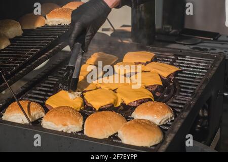 Preparar hamburguesas de queso o hamburguesas con bollos de pan en una parrilla de carbón caliente al aire libre. Detalle de deliciosas y jugosas hamburguesas caseras.