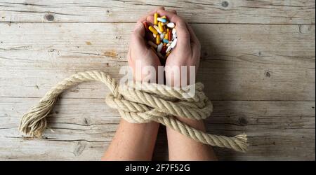 Las manos del hombre están atadas con una cuerda y en sus manos sostiene muchas píldoras diferentes, adicción al concepto, adicción a las drogas, foto tomada de arriba Foto de stock