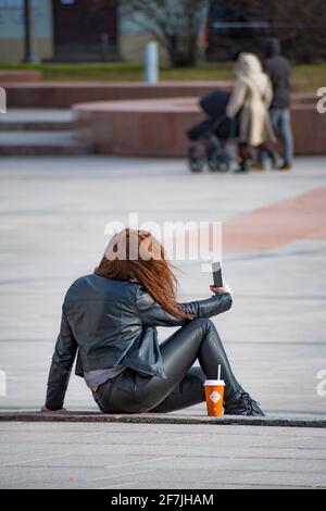 Chica tomando selfie o video chateando o llamando sosteniendo un smartphone en la ciudad, vertical Foto de stock