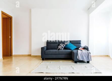 Sofá sencillo en una habitación espaciosa sin decoración, paredes blancas minimalistas con gran iluminación. Foto de stock