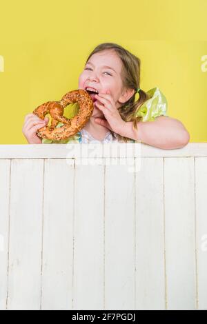 Concepto de vacaciones de la Oktoberfest bávara alemana. Sonrisa graciosa linda niña pequeña rubia caucásica niño en vestido tradicional con pasteles pretzel, en