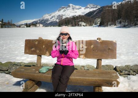 Congelación Vacaciones de invierno - jóvenes felices y hermoso asiático coreano mujer en el banco en el paisaje helado del lago rodeado de nieve Montañas disfrutando de Suiza