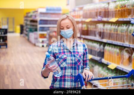 Mujer con máscara de compra segura de comestibles en medio de la pandemia de coronavirus en el supermercado.