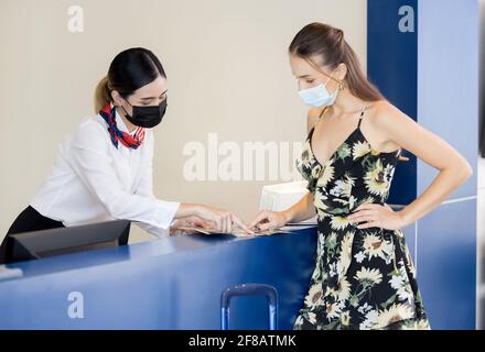 La recepcionista entrega un pasaporte a un turista en te recepción y recepción de un albergue Foto de stock