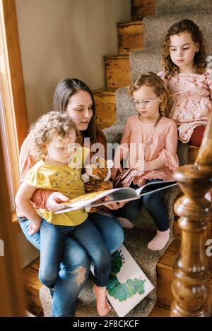 Una madre joven y sus tres niñas sentadas en la escalera libros de lectura de casos