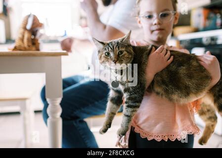 Pequeña niña sosteniendo su lindo gato mascota en ella brazos en la cocina