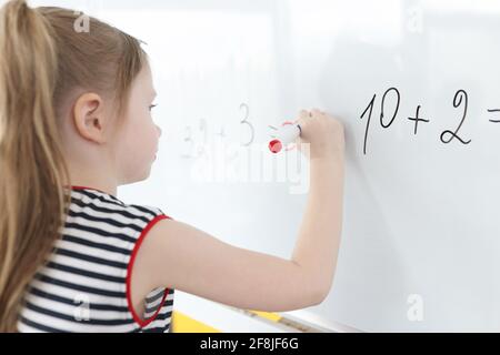 La niña escribe ejemplos de matemáticas en pizarra blanca Foto de stock
