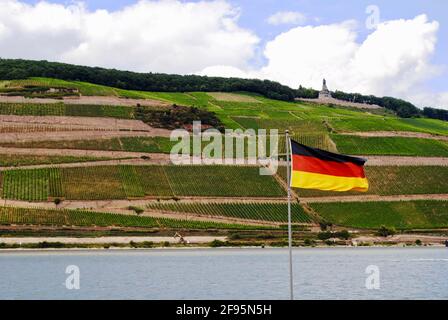 Río Rin, bandera alemana y viñedos. Niederwalddenkmal, estatua de Germania, monumento a la reunificación se encuentra en la colina en Rüdesheim am Rhein, Alemania Foto de stock
