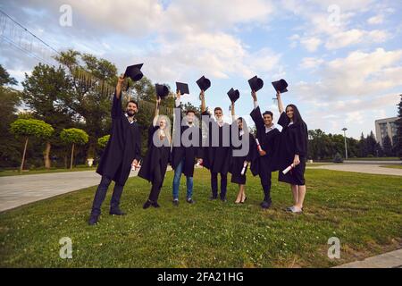 Grupo de felices graduados universitarios de pie con diplomas y holding bonetes en manos elevadas Foto de stock