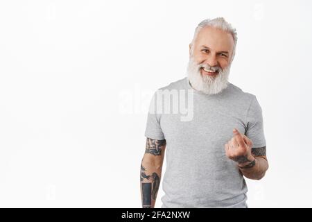 Acércate más. Feliz hombre viejo guapo con tatuajes atraen a acercarse, dedo de la mano, sonriendo y riendo mientras que atrae a la gente, invitando ir con él Foto de stock