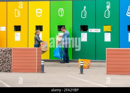 Gran estación de eliminación de residuos separada con marcas de color cerca del aparcamiento con hombre y mujer depositando basura en San Petersburgo, Rusia Foto de stock