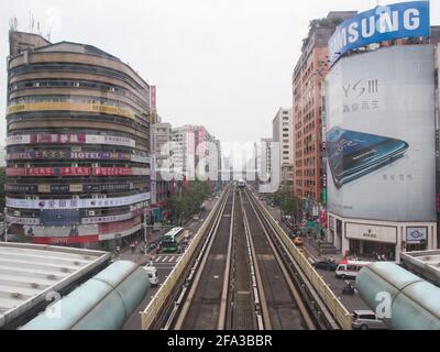 La vista desde el frente de un metro, el metro elevado tren suburbano por las vías entre edificios de oficinas en un día vaga, lleno de humo. En Taipei, Taiw Foto de stock