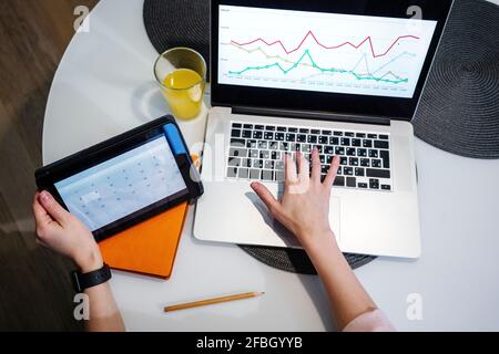 Mujer realizando cálculo en tableta digital mientras trabaja en gráfico en el portátil en casa Foto de stock