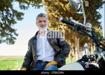 Hombre sonriente con chaqueta biker sentado en la motocicleta Foto de stock