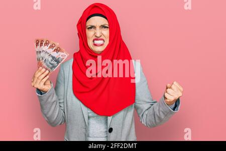 Una hermosa mujer hispana que llevaba hijab islámico con billetes de dólares australianos irritada y frustrada gritando con ira, gritando loca con ang Foto de stock