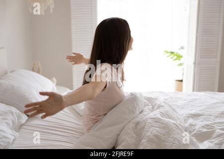 Una adolescente se despertando en la cama, estirando los brazos después de dormir bien