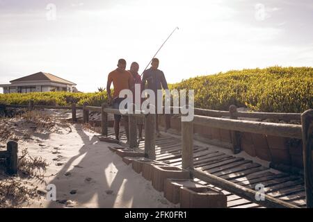 Padre afroamericano y sus dos hijos con cañas de pescar caminando juntos en el puente Foto de stock