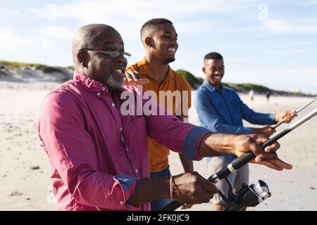 Padre afroamericano y sus dos hijos con cañas de pescar pesca juntos en la playa Foto de stock