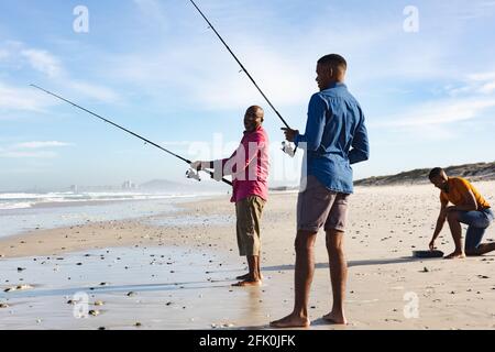 Padre afroamericano y sus dos hijos con cañas de pescar pesca juntos en la playa Foto de stock