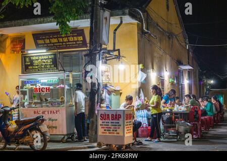 Las familias vietnamitas se sentaron afuera por la noche comiendo comida callejera, Hoi An, Vietnam Foto de stock