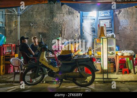 Los hombres vietnamitas escalofriando en la zona de comida al borde de la carretera por la noche, Hoi An, Vietnam Foto de stock
