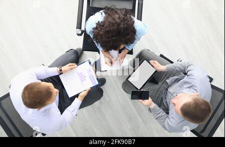 La gente de negocios se sienta en sillas con tableta y negocios comerciales vista superior de gráficos y discusión de planes de trabajo Foto de stock