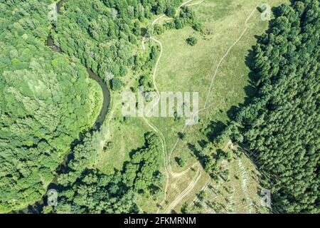 bosque con un río serpenteante y prado con camino de tierra y rastros de actividad humana. vista aérea desde arriba Foto de stock