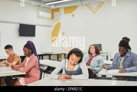Vista de amplio ángulo en diversos grupos de estudiantes sentados en escritorios en clase escolar con enfoque en la joven mujer afroamericana en frente, espacio de copia