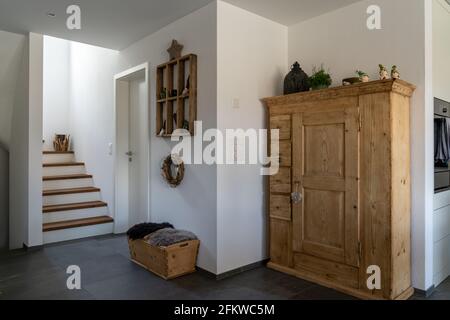Una vista interior de un pasillo elegante y escaleras con pisos de baldosas negras y paredes de yeso blanco y muebles de madera y artículos decorativos Foto de stock