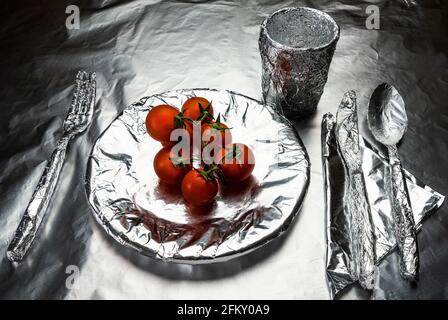 placa de inicio, vajilla y un vaso cubierto con papel de aluminio con algunos tomates Foto de stock