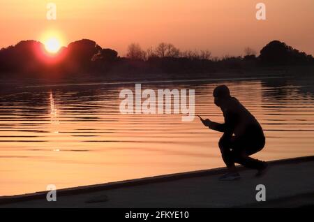 Hombre con smartphone en la mano al atardecer en el río