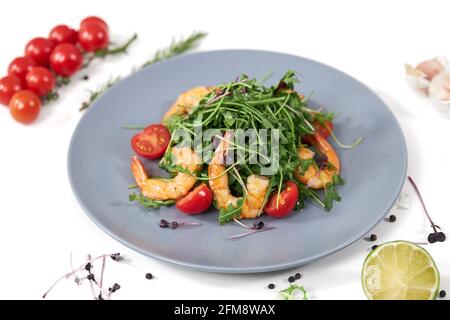 Primer plano de una apetitosa ensalada con rúcula fresca, tomates cherry y jugosos camarones sobre fondo blanco. Concepto de menú con los productos adecuados para la pérdida de peso. Foto de stock
