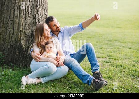 Hacer recuerdos familiares. Feliz padres mamá y papá con hija niña tomando foto selfie con cámara de smartphone en el parque.