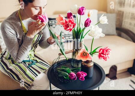 Mujer hace arreglos florales de tulipanes en el jarrón en casa. Florería huele flores recogidas en la cesta. Interior y decoración acogedora Foto de stock