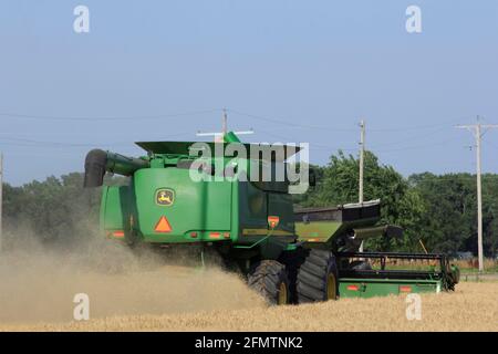 John Deere combina el corte de trigo con el polvo de trigo en el aire en un campo agrícola en el país de Kansas.