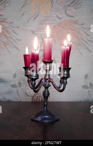 candelabro de estaño con velas rojas y tapices florales en el fondo Foto de stock
