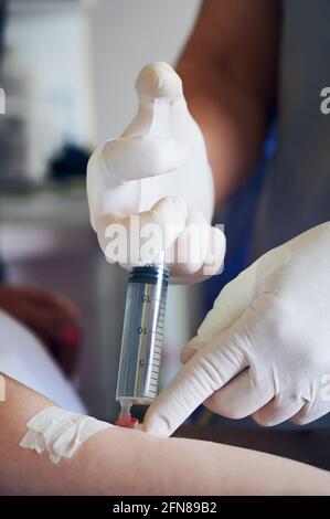 Primer plano de las manos del trabajador médico con guantes estériles inyectando dosis de anestesia con jeringa. El médico inserta la aguja en el brazo del paciente mientras se inyecta el medicamento anestésico antes de la cirugía. Foto de stock