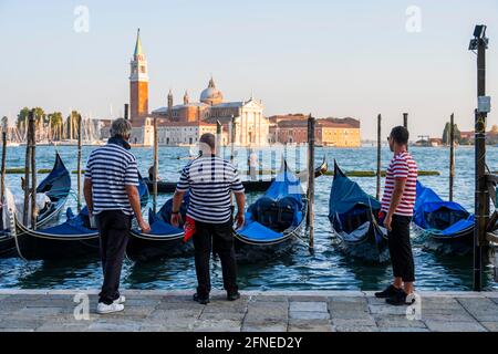 Tres gondoleros, gondolieri, frente a las góndolas venecianas en la laguna de Venecia, en la parte trasera de la iglesia San Giorgio Maggiore, Venecia Foto de stock