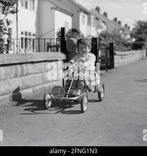 1959, histórico, fuera en la calle en un pavimento, una joven sentada en un coche de juguete a pedales con marco metálico, un Tri-Ang 7 Go Kart, Inglaterra, Reino Unido. Iniciado en 1919, Tri-ang toys era el nombre de marca de Lines Brothers, compan de juguetes británico, que en un momento dado alrededor de finales de 1950, se cree que es el negocio de juguetes más grande del mundo. Se plegaron en 1971. Foto de stock